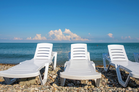 White chaise lounges on the rocky beach, blue cloudy sky background
