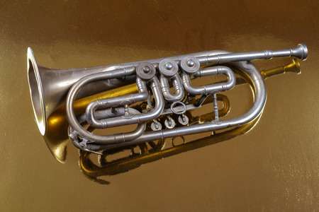 Old silver trumpet reflected on a golden background