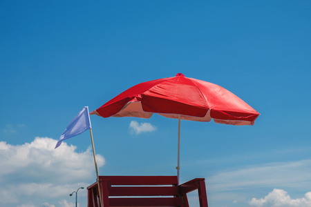red beach umbrella and white flag, blue sky backgroundの写真素材