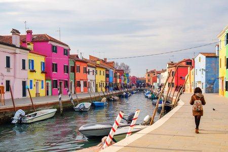 A girl taking a walk in the street across Burano island canal, colorful houses and cloudy skyのeditorial素材