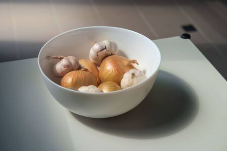 Onions and garlic in the white porcelain cup on the table