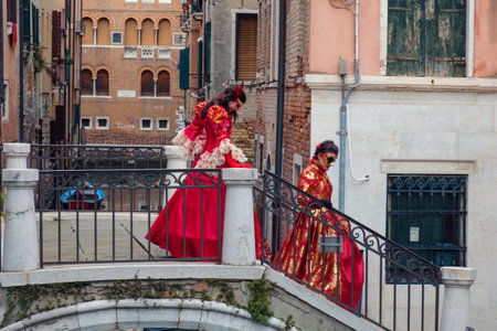 Venice, Italy, February 24, 2019: Masked couple in red dresses on the bridge,のeditorial素材