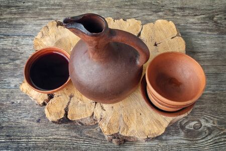 A traditional Georgian wine jug and clay cups filled with a red wine on the wooden tableの写真素材