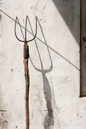 Rusty well used garden fork on the grunge wall with drop shadowの写真素材