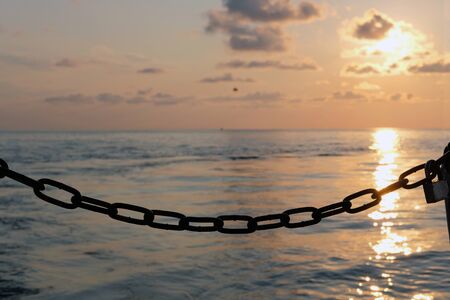 Silhouette of a chain and lock with sunset sea background, selective focusの写真素材