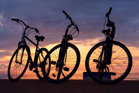 The silhouette of bikes, row of bikes on the beach with sunset cloudy sky backgroundの写真素材