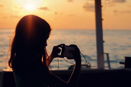 Silhouette of a girl taking pictures of the sunset landscape
