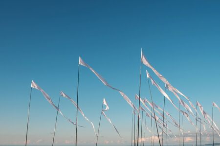 White waving flags on the beach, blue sky background