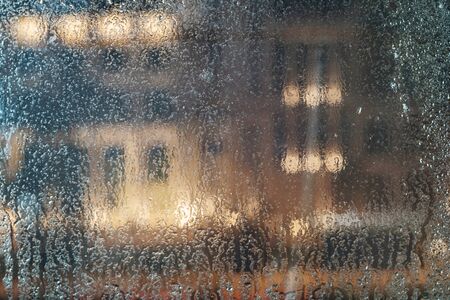 Condensation and rain drops on the wet glass window, blurred illuminated background