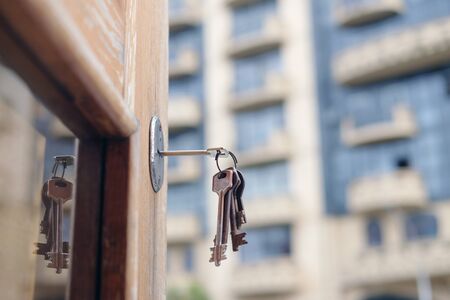 Set of old keys in the keyhole reflecting on the glass of door frame, blurred building backgroundの写真素材