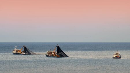 Tree fishing trawler at the blue sea catching a fish, colorful sunrise sky background  