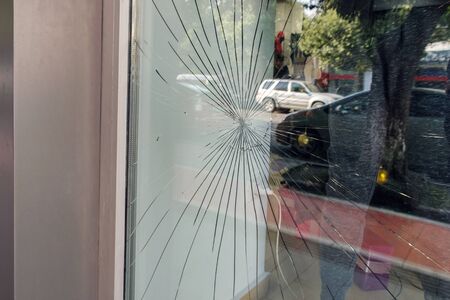 Cracked glass on the a shop's window reflecting a view of the street 