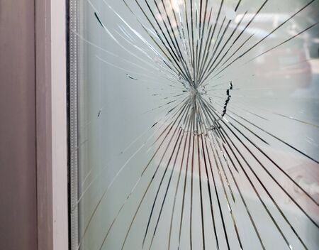 Cracked glass on the a shop's window reflecting a view of the street 
