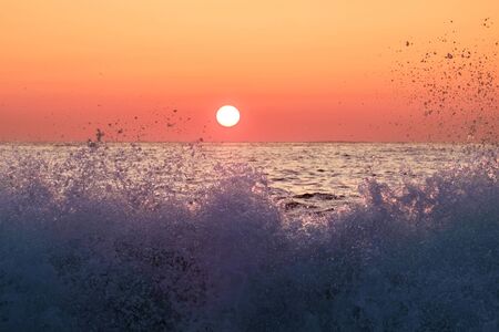 Sunset and colorful orange sky behind splashing wavesの写真素材