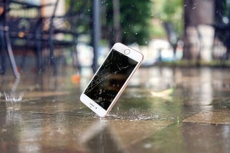 White smartphone falling and crashing on wet ground in the city park on a rainy day. accident with smartphoneの写真素材