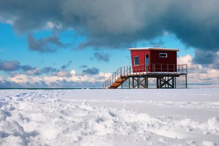 Red lifeguard tower or rescue tower on the snow covered beach, beautiful cloudy sky backgroundの写真素材