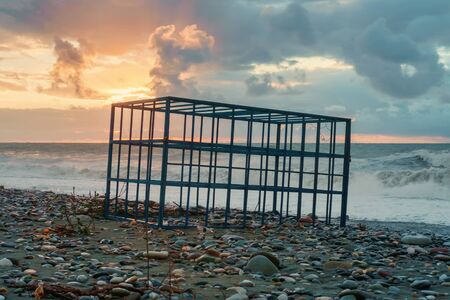 Empty metal cage on the sunset rocky beachの写真素材