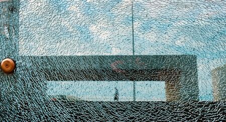 View of a bench and walking man at the sea side park behind the cracked textured glass