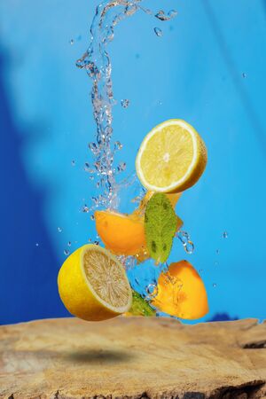 Falling fresh slices of the lemon with fresh water in the air over the wooden board. Flying fruits concept on blue background の写真素材