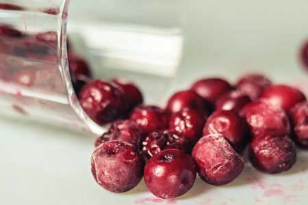 Closeup of frozen cherry in the glass on white surface. Selective focus