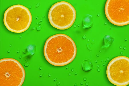 Fresh juicy slices of orange and lemon on bright green background covered with water drops. Creative food background, top viewの写真素材