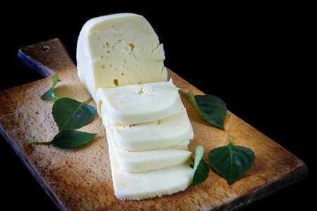 Sliced cheese on old wooden board with black background. Georgian cheese sulguni