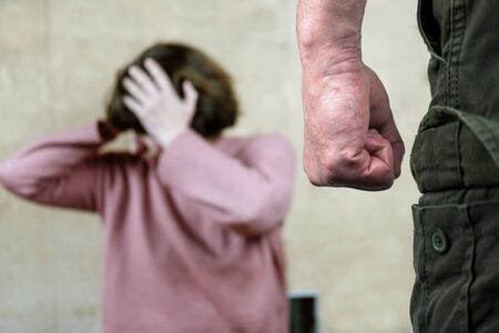 A man's clenched fist threatening with blurred view of unhappy crying woman covering her face on the background. domestic violence conceptの写真素材