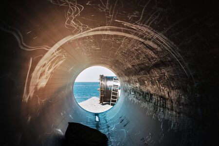Industrial landscape, view of the sea and the end of the large tube from the inside of a scratched tube pipeの写真素材