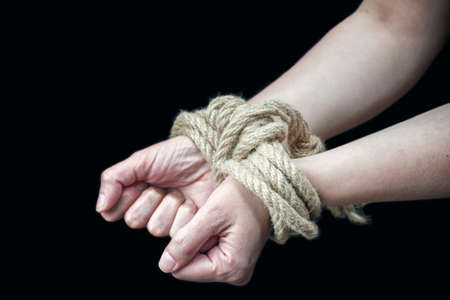 Hands of a victim woman tied up with rough rope on the black background. Stop abusing violence...
