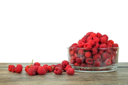 Fresh raspberries in a glass bowl on a wooden table with isolated white background