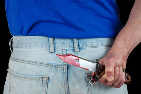 Hand holding and hiding a bloody hunter's knife. Red blood is pouring on the hand and knifeの写真素材