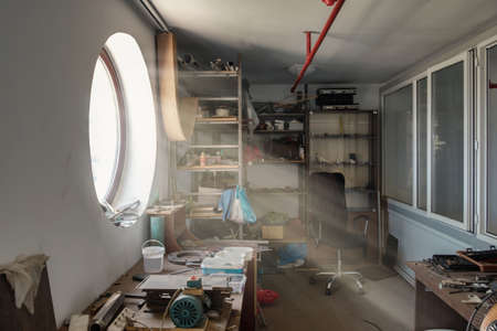 Interior of a small room with tools lit by sun rays penetrating through a round windowの写真素材
