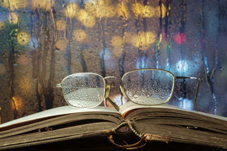 Glasses and open book on the window sill with night illuminated background, selective focusの写真素材