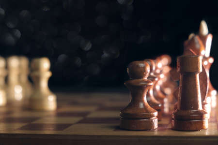 Wooden chess pieces and a chessboard on blurred dark background, selective focusの写真素材