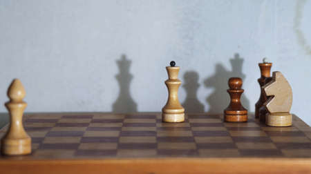 Wooden chess pieces and a chessboard with drop shadows on the wall, selective focus