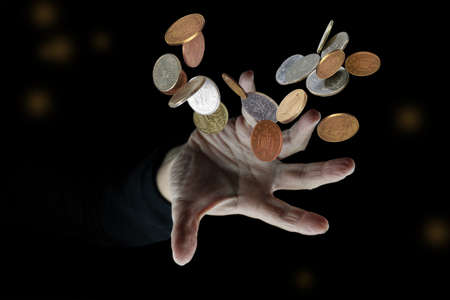 Hand throwing various money coins on blurred dark background, selective focusの写真素材