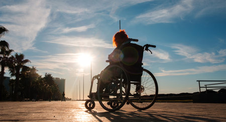 Disabled girl with red hair in a wheelchair at the sunset sea side parkの写真素材