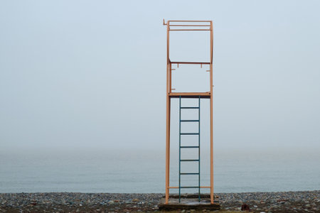 Yellow metal lifeguard tower on the puddle beach with misty sea and sky backgroundの写真素材