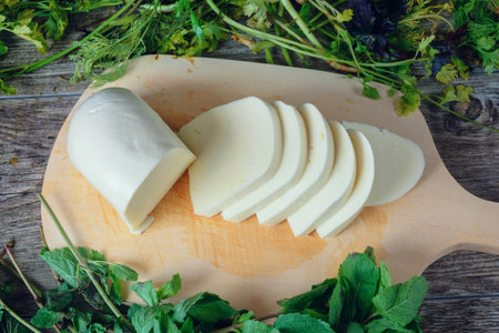 Sliced cheese on a wooden table with green herbs background. Georgian cheese sulguni