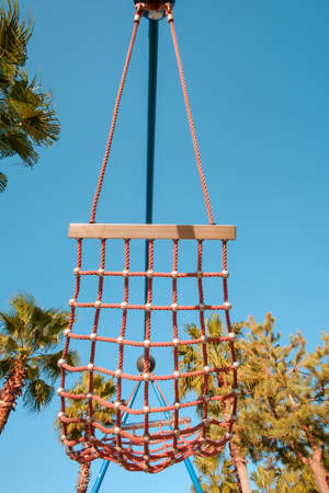 Red hammock made of rope on a blue sky and trees backgroundの写真素材