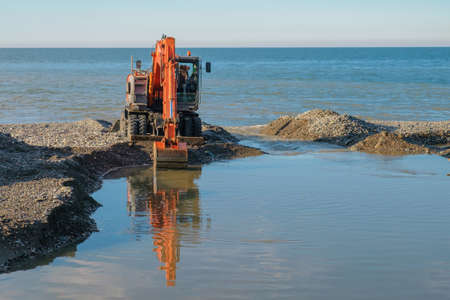 Large tracked excavator digging and cleaning channel at the coastの写真素材