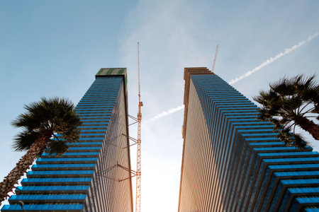 Bottom view of modern skyscrapers and constructing cranes against blue sky
