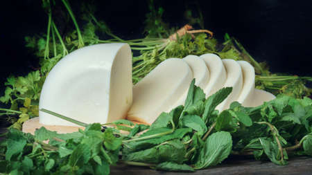 Sliced cheese on a wooden board with green herbs background. Georgian cheese sulguniの写真素材