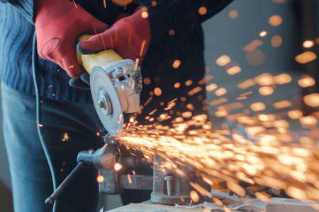 Worker working with a circular grinder on a metal with sparks flying out of them, selective focus