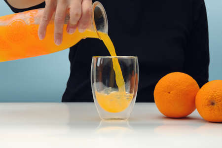 Female hand holding glass jar of fresh squeezed orange juice and pouring. selective focusの写真素材