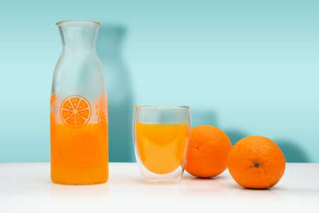 Ripe oranges, a glass bottle and mug with f fresh squeezed orange juice on white background.