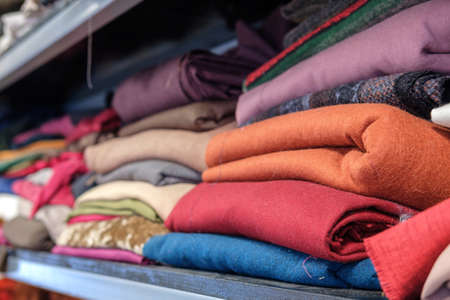 Multicolored various clothes stacked in piles on a shelf in a atelier, selective focus