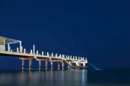 Night fishing on the pier, fisherman with flashlights on the pier with starry sky backgroundの写真素材