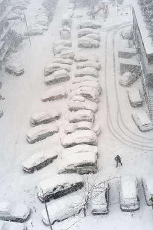 A row of parked cars covered with snow during heavy snowfall, top view