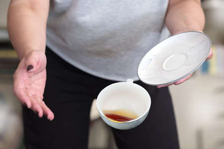 A female in gray t-shirt dropping teacup with tea, selective focusの写真素材